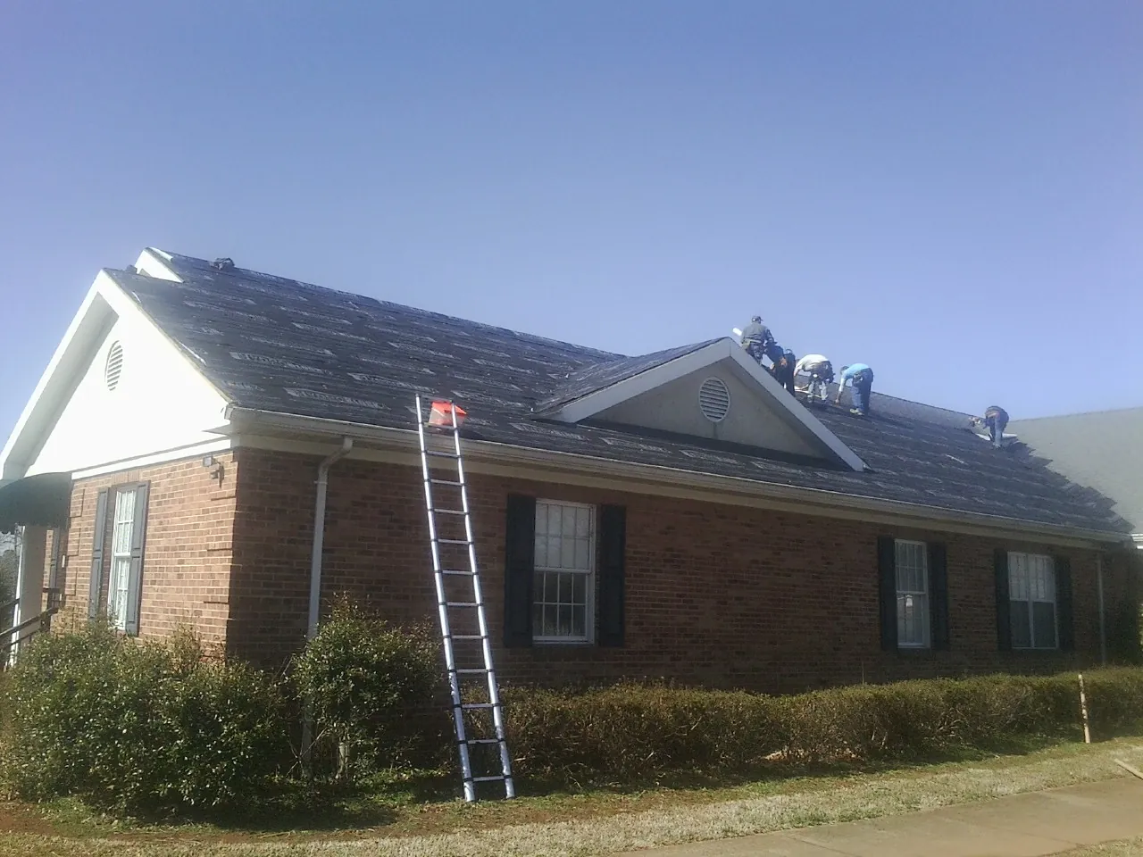 Crew tearing shingles off a brick ranch roof with a ladder set — Metal Roof Repair work by our crew in Tower City