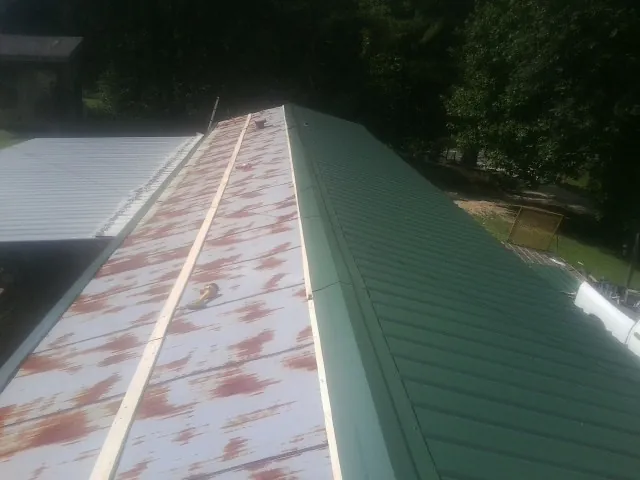 Old rusted panels beside newly installed green metal roofing — Wind Damage Roof Repair by Roofing Brothers in Tower City