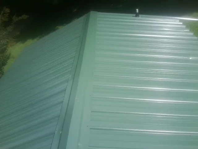 New green metal panels meeting at the ridge of a roof — Flat Roof Repair work by our crew in Tower City
