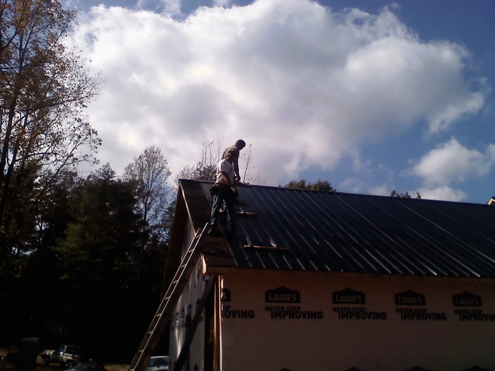 Roofer fastening dark metal panels high against a cloudy sky, from a Roof Inspection job in Tower City
